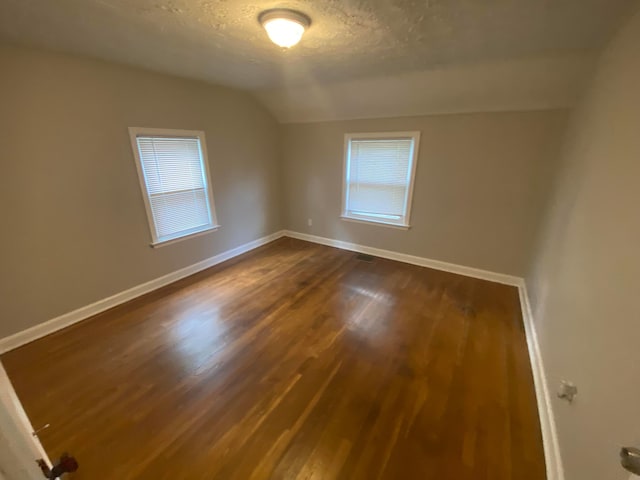 empty room with plenty of natural light, dark hardwood / wood-style flooring, lofted ceiling, and a textured ceiling