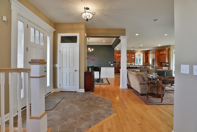 entrance foyer with light wood-type flooring, ornate columns, a notable chandelier, and crown molding