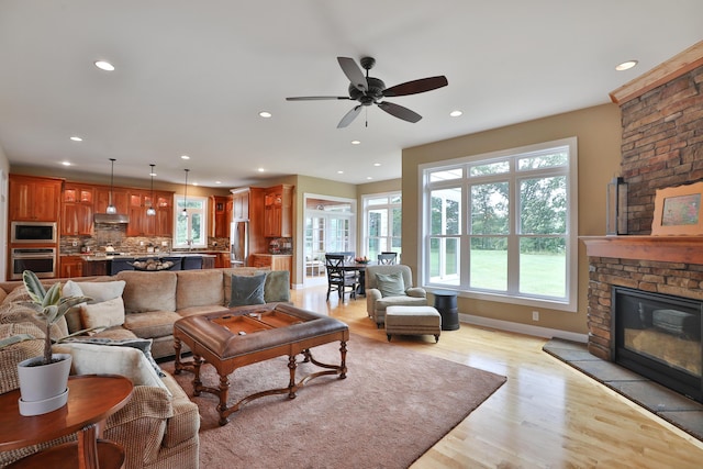 living room with a stone fireplace, ceiling fan, a healthy amount of sunlight, and light wood-type flooring