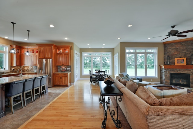 living room with light hardwood / wood-style floors, a stone fireplace, ceiling fan, and a healthy amount of sunlight