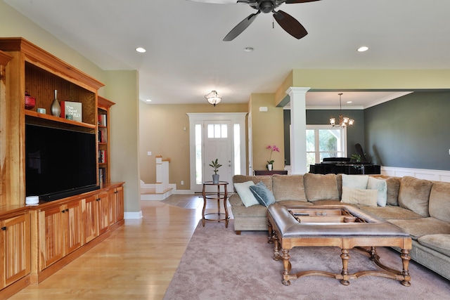 living room with ceiling fan with notable chandelier, light wood-type flooring, and crown molding