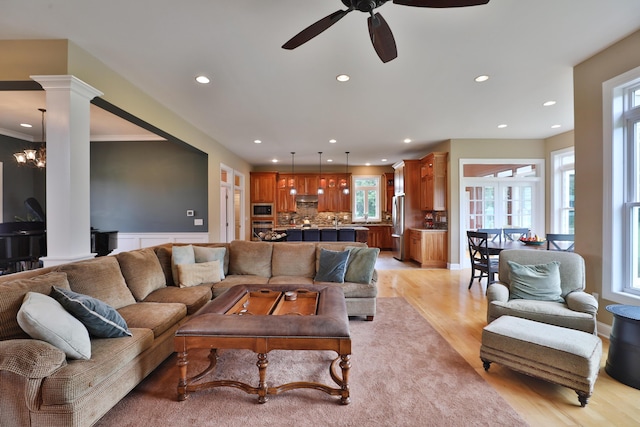 living room with ceiling fan with notable chandelier, light hardwood / wood-style floors, decorative columns, and ornamental molding