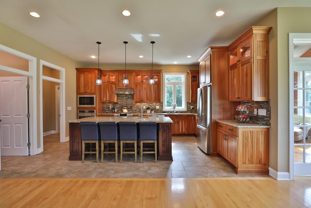 kitchen featuring light stone countertops, a center island with sink, light hardwood / wood-style floors, and appliances with stainless steel finishes