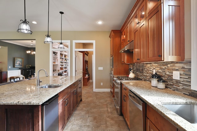 kitchen featuring pendant lighting, a large island with sink, sink, light stone countertops, and appliances with stainless steel finishes