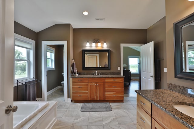 bathroom with a washtub, vanity, toilet, and vaulted ceiling