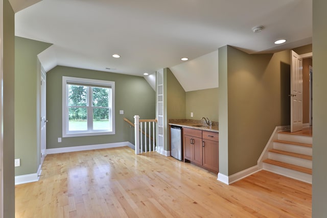 bar with light stone countertops, vaulted ceiling, sink, light hardwood / wood-style flooring, and dishwasher