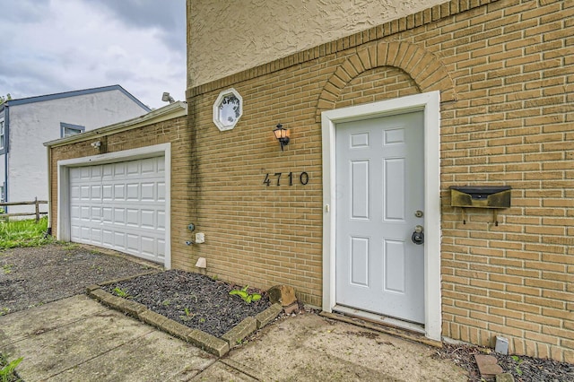 doorway to property featuring brick siding, an attached garage, and driveway