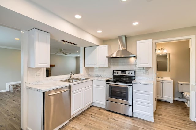 kitchen featuring appliances with stainless steel finishes, wall chimney range hood, a sink, white cabinetry, and decorative backsplash