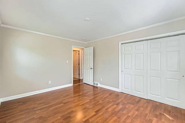 unfurnished bedroom featuring crown molding, wood finished floors, baseboards, and a closet