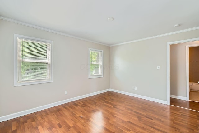 empty room with crown molding, wood finished floors, baseboards, and a smoke detector