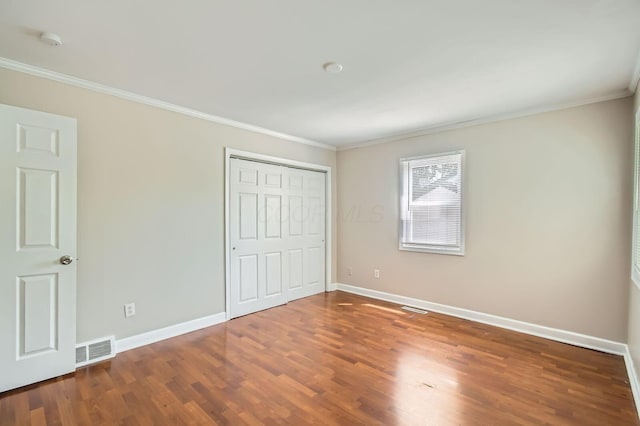 unfurnished bedroom featuring crown molding, wood finished floors, baseboards, and a closet