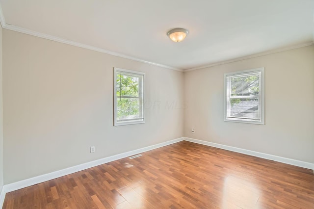 spare room with crown molding, healthy amount of natural light, baseboards, and wood finished floors