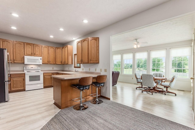 kitchen featuring kitchen peninsula, a kitchen bar, light wood-type flooring, white appliances, and sink