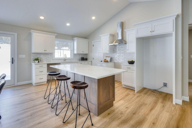 kitchen featuring white cabinets, a center island, lofted ceiling, a kitchen breakfast bar, and wall chimney range hood