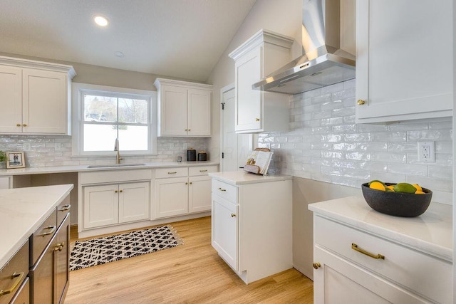 kitchen with wall chimney range hood, lofted ceiling, light wood-type flooring, white cabinets, and sink