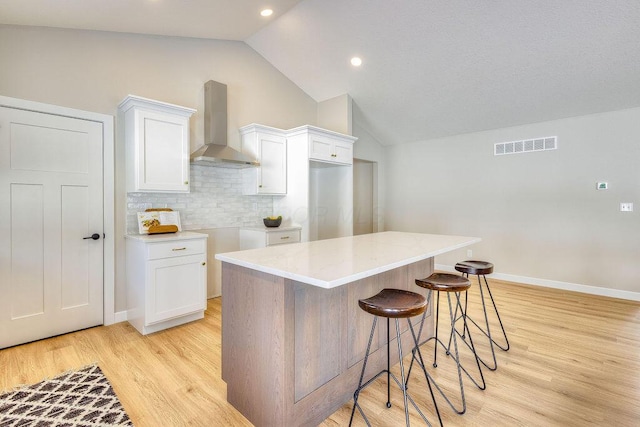 kitchen with wall chimney exhaust hood, a center island, light hardwood / wood-style floors, decorative backsplash, and white cabinets