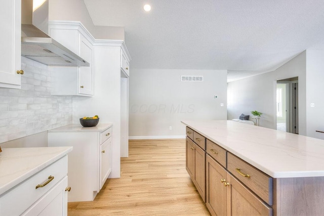 kitchen with light wood finished floors, tasteful backsplash, visible vents, wall chimney exhaust hood, and light stone counters