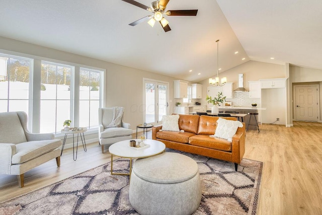 living area with lofted ceiling, light wood finished floors, and ceiling fan with notable chandelier