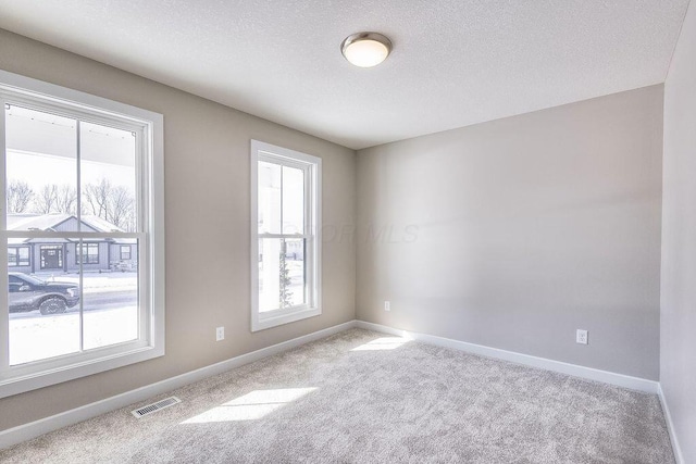 carpeted empty room with baseboards, visible vents, and a textured ceiling