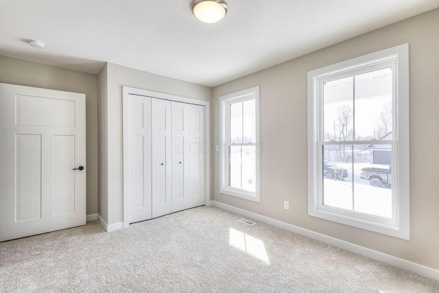 unfurnished bedroom with a textured ceiling, visible vents, baseboards, a closet, and carpet