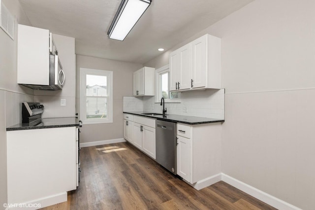 kitchen featuring appliances with stainless steel finishes, dark stone counters, sink, white cabinets, and dark hardwood / wood-style floors