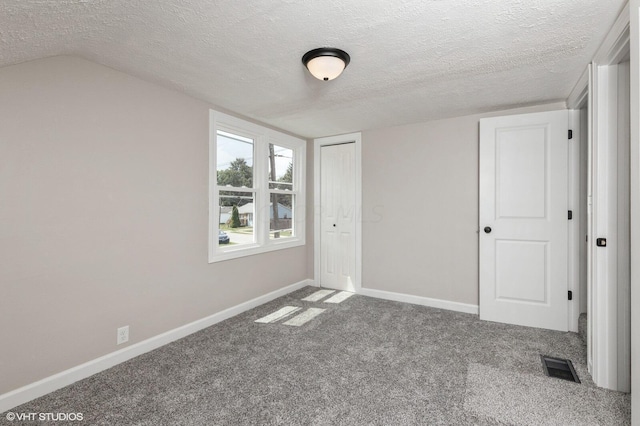 unfurnished bedroom with carpet flooring, a textured ceiling, vaulted ceiling, and a closet