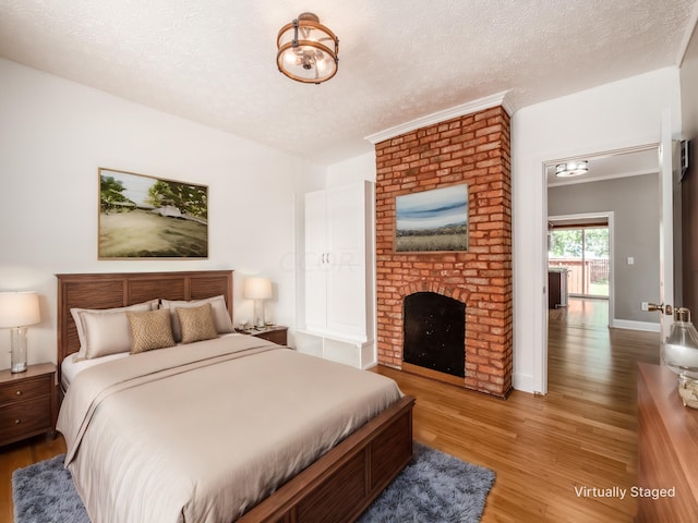 bedroom with light hardwood / wood-style floors, a textured ceiling, and a brick fireplace