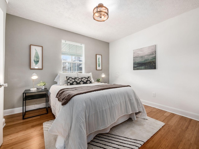 bedroom with baseboards, light wood-type flooring, and a textured ceiling