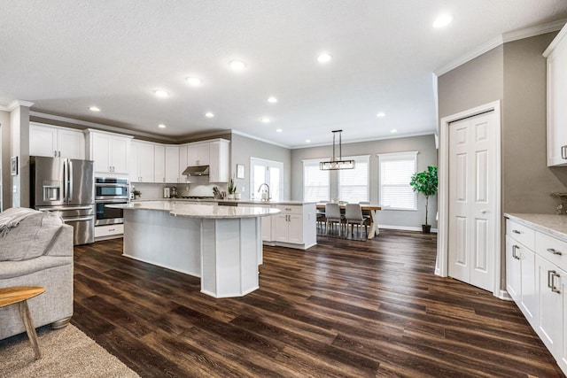 kitchen with light stone countertops, appliances with stainless steel finishes, crown molding, dark hardwood / wood-style floors, and hanging light fixtures