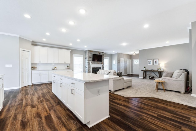 kitchen with light stone countertops, a kitchen island, dark hardwood / wood-style flooring, crown molding, and white cabinets