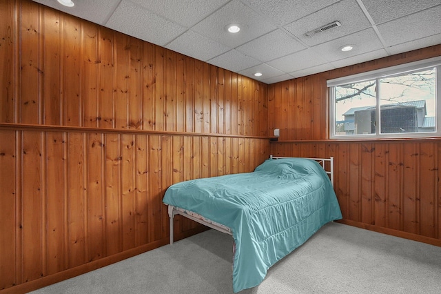 bedroom featuring light colored carpet, wooden walls, and a paneled ceiling