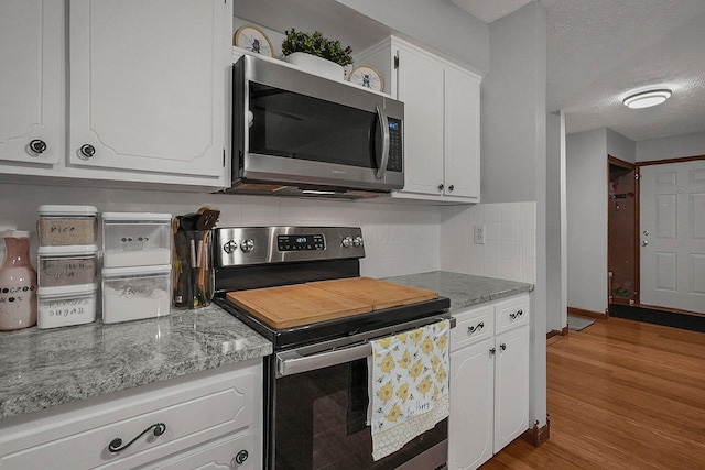 kitchen with appliances with stainless steel finishes, white cabinets, light hardwood / wood-style floors, and decorative backsplash