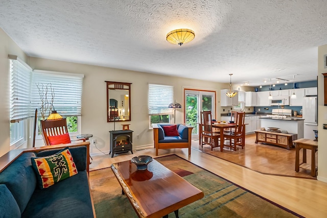 living room with light hardwood / wood-style floors, a wood stove, and a textured ceiling