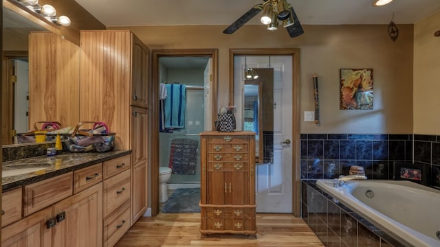 bathroom with tiled tub, toilet, vanity, and hardwood / wood-style flooring