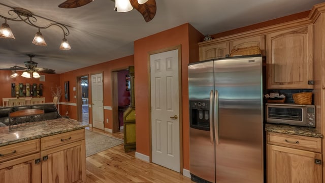 kitchen with pendant lighting, dark stone counters, light hardwood / wood-style flooring, ceiling fan, and stainless steel fridge