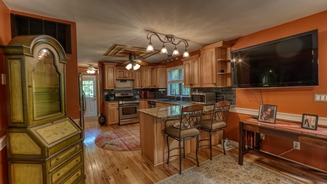 kitchen with sink, stainless steel stove, decorative backsplash, light wood-type flooring, and a kitchen bar