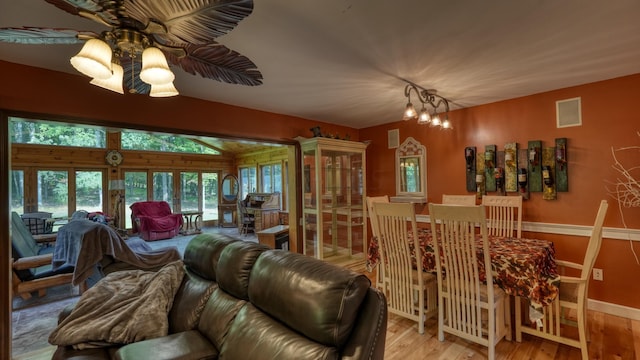 living room with ceiling fan with notable chandelier, light wood-type flooring, and vaulted ceiling