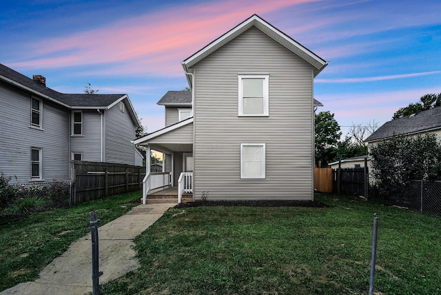 back of property at dusk featuring a lawn, a porch, and fence private yard