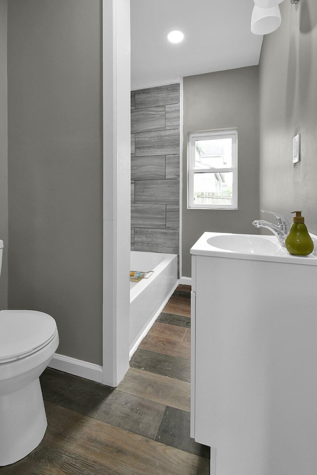 full bath with baseboards, toilet, a tub to relax in, wood finished floors, and a sink