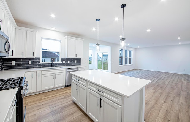 kitchen with white cabinets, a center island, appliances with stainless steel finishes, and light hardwood / wood-style flooring