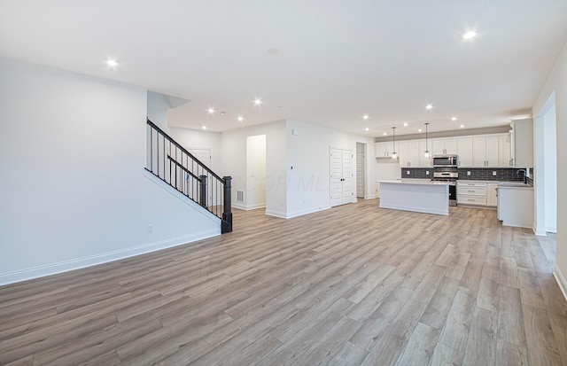 kitchen with white cabinets, a kitchen island, light wood-type flooring, and appliances with stainless steel finishes