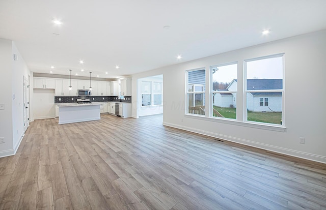 kitchen with stainless steel appliances, a kitchen island, pendant lighting, light hardwood / wood-style flooring, and white cabinetry