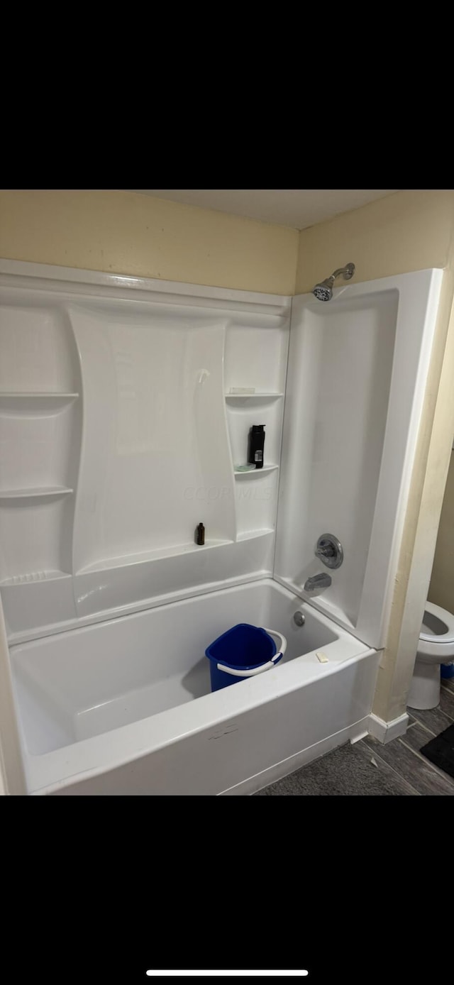 bathroom with washtub / shower combination, hardwood / wood-style flooring, and toilet