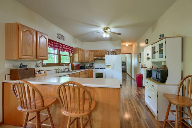 kitchen with kitchen peninsula, white appliances, sink, light hardwood / wood-style floors, and a breakfast bar area