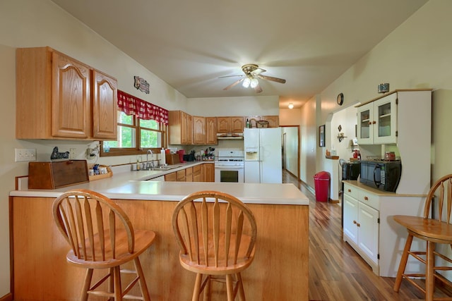 kitchen featuring hardwood / wood-style flooring, a kitchen breakfast bar, white appliances, and kitchen peninsula