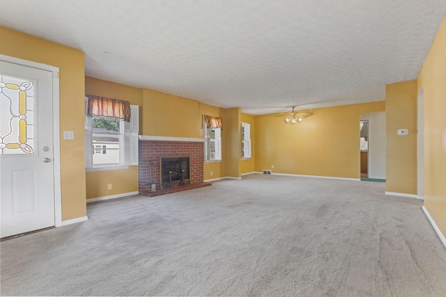 unfurnished living room with ceiling fan, carpet floors, a textured ceiling, and a brick fireplace