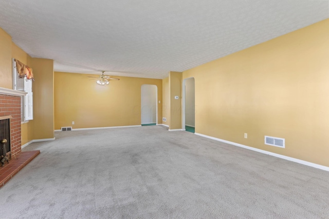 unfurnished living room featuring carpet, ceiling fan, a textured ceiling, and a brick fireplace