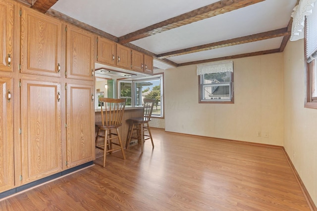 kitchen with beamed ceiling, a breakfast bar, and light hardwood / wood-style flooring