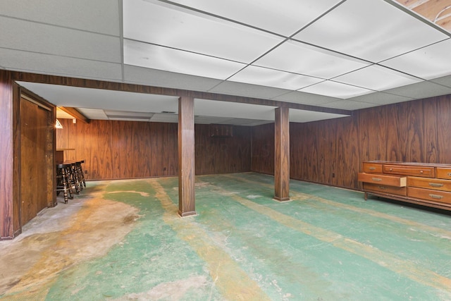 basement featuring a paneled ceiling and wooden walls