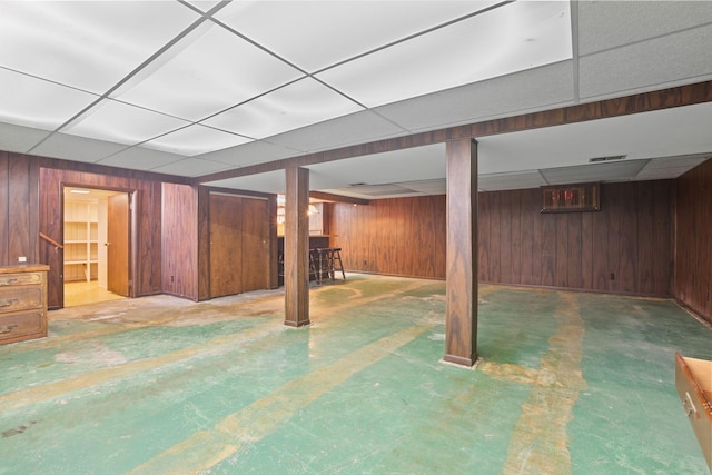 basement featuring a drop ceiling and wooden walls